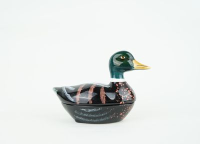 un petit canard noir et doré posé sur une surface blanche