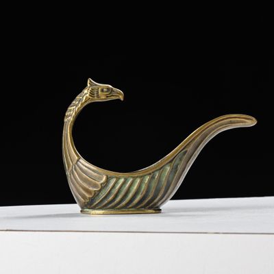 une image représentant un objet en forme d'oiseau de couleur dorée posé sur une table blanche