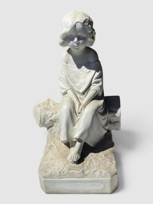 statue d'un garçon assis sur un rocher, un livre à la main