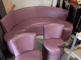 un canapé violet incurvé et deux tabourets dans une pièce