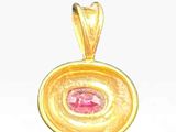 a close up of a gold pendant with a pink stone