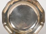 assiette en argent plaqué aux bords festonnés, posée sur un socle, sur fond blanc