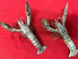 une paire de peignes à cheveux en forme de pince de homard en argent, posés sur un tissu rouge