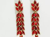 une paire de boucles d'oreilles rouges et dorées posées sur une surface blanche
