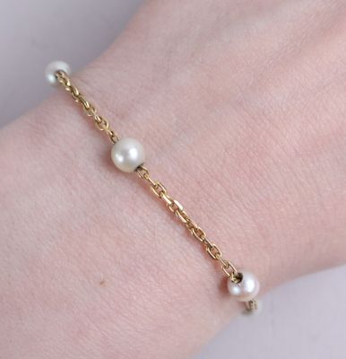 a close up of a person ' s hand wearing a gold bracelet with pearls