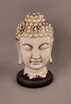 statue représentant une tête de Bouddha posée sur un socle en bois, avec un fond gris