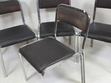 four black chairs and a stool in a room with a white wall