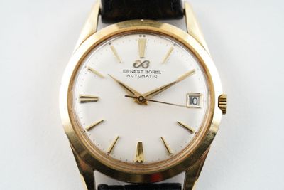 une montre-bracelet en or avec un cadran blanc sur un bracelet en cuir noir