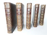 four old books are lined up in a row on a white surface