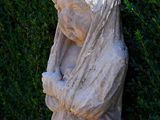 a statue of a woman that is standing in front of a bush