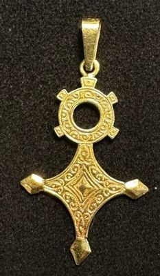 an image of a gold cross pendant on a black surface