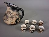 six cups and a pitcher sitting next to each other on a table