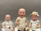 trois poupées représentant des bébés, assises les unes à côté des autres sur une table