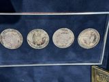four silver coins in a glass display case on a blue surface