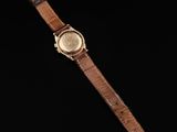 a gold watch with a brown leather strap on a black background