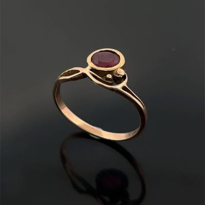 a gold ring with a red stone on a black surface