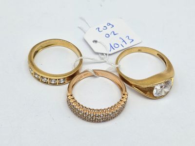 three gold rings with diamonds on a white surface