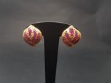 une paire de boucles d'oreilles roses et dorées posées sur un support noir