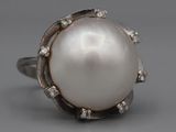 an image of a white pearl and diamond ring on a gray background