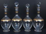 four glass decanters with gold trims on a black surface
