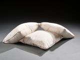 two white pillows sitting on top of each other on a gray floor