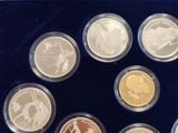six silver and gold coins in a blue box with a ticket