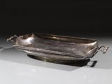 une assiette en argent antique avec une poignée sur une surface blanche