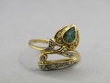gros plan d'une bague en or avec une pierre verte et des diamants