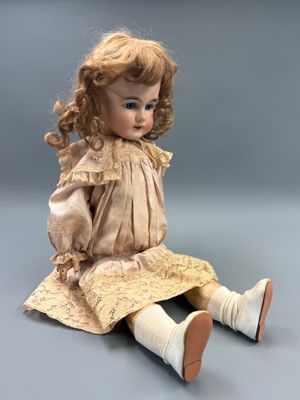 une poupée ancienne assise par terre, les jambes croisées