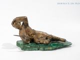 bronze statue of a man laying on a rock with a sword
