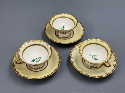 trois tasses et soucoupes aux bords dorés sur un fond gris