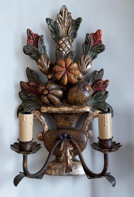 une applique murale sur laquelle sont posées deux bougies et une corbeille de fruits