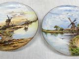 two plates with windmills painted on them sitting on a table