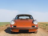 an orange porsche parked on a dirt road in the middle of a field