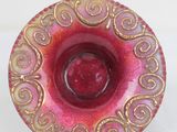 a red and gold bowl on a stand on a white surface