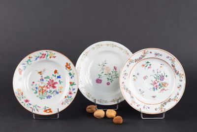 trois assiettes ornées de fleurs et de noix, posées sur un fond noir