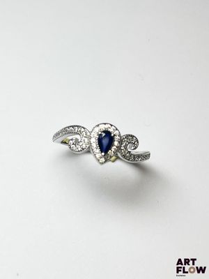 un gros plan d'une bague en forme de cœur sertie de diamants et de saphirs, posée sur une surface blanche