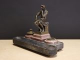 a bronze statue of a man sitting on top of a suitcase
