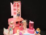 un petit bateau rose avec des poupées Barbie dessus, posé sur une surface noire