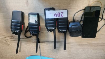 four walkie talkies are lined up on a table next to a cell phone