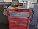 une boîte à outils rouge sur laquelle est posé un ordinateur portable, devant une fenêtre