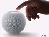 une personne montrant du doigt une enceinte HomePod blanche posée sur une surface blanche