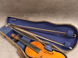 un violon orange repose dans un étui bleu posé sur une surface blanche