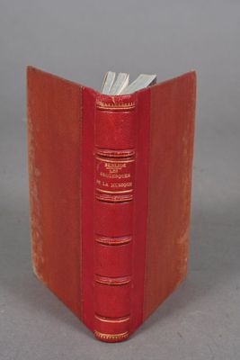 an old red book sitting on top of a table next to a gray wall
