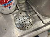 a metal sink with a metal strainer and a bottle of deter