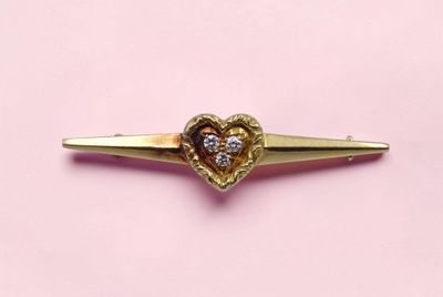 un gros plan d'une broche dorée en forme de cœur sur fond rose