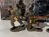 three figurines of men in military uniforms are posed in front of a poster