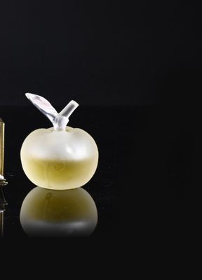 a bottle of perfume next to an apple on a black surface