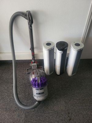 un aspirateur posé par terre à côté de quelques rouleaux de papier toilette