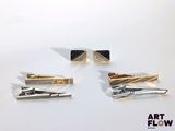 trois pinces à cravate dorées et noires posées sur une surface blanche